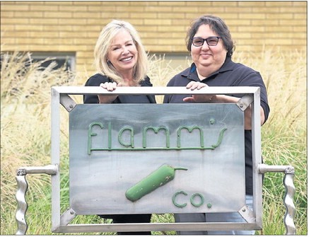 Photo of Gina Flamm and Dorothy Munao standing outside Flamm Pickle & Packing, posed behind a metal sign that reads ‘Flamm’s Co.’